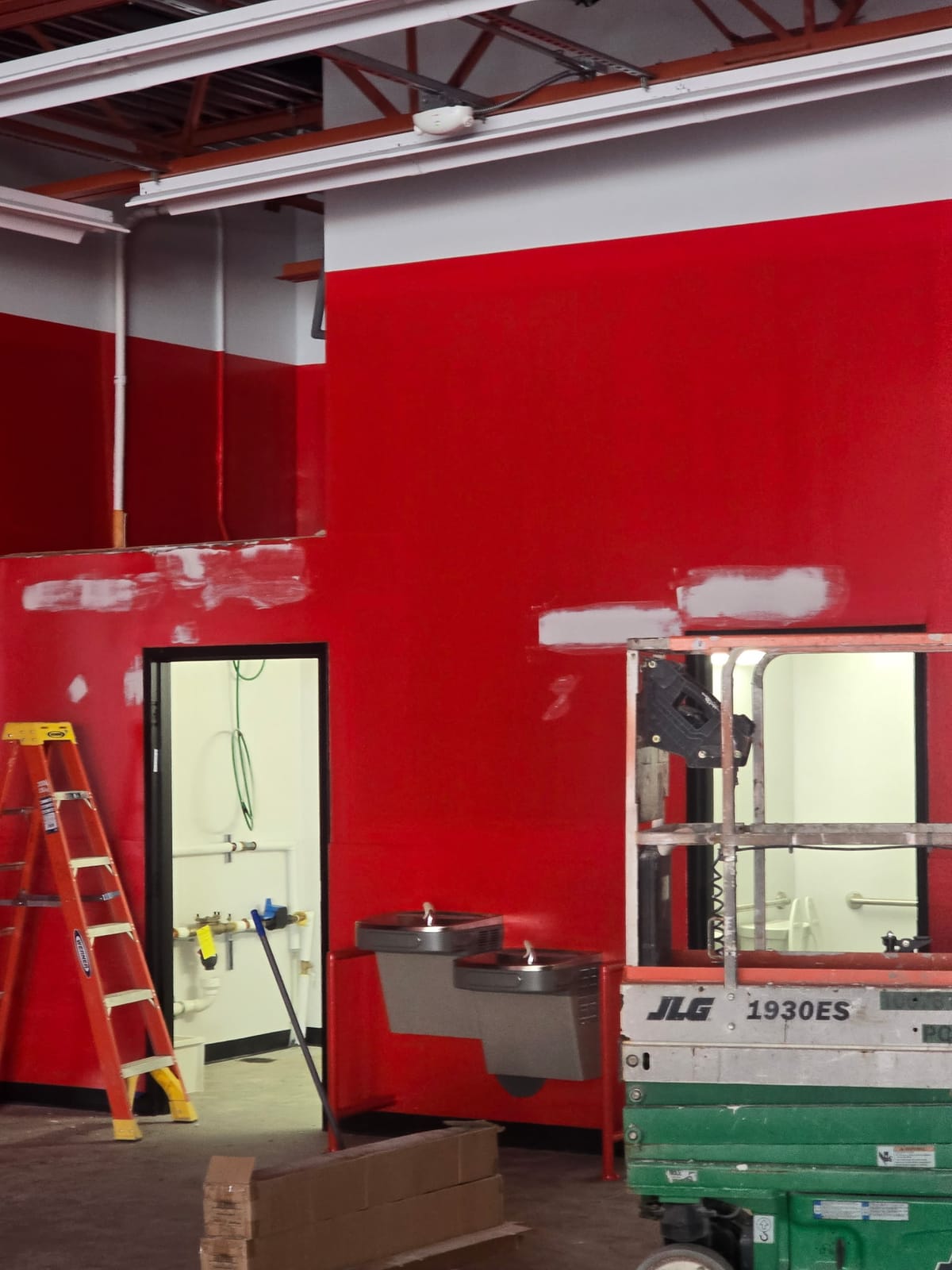 Interior of a new AutoZone under construction with freshly painted red walls, exposed steel joists, a scissor lift and a step ladder still on the floor