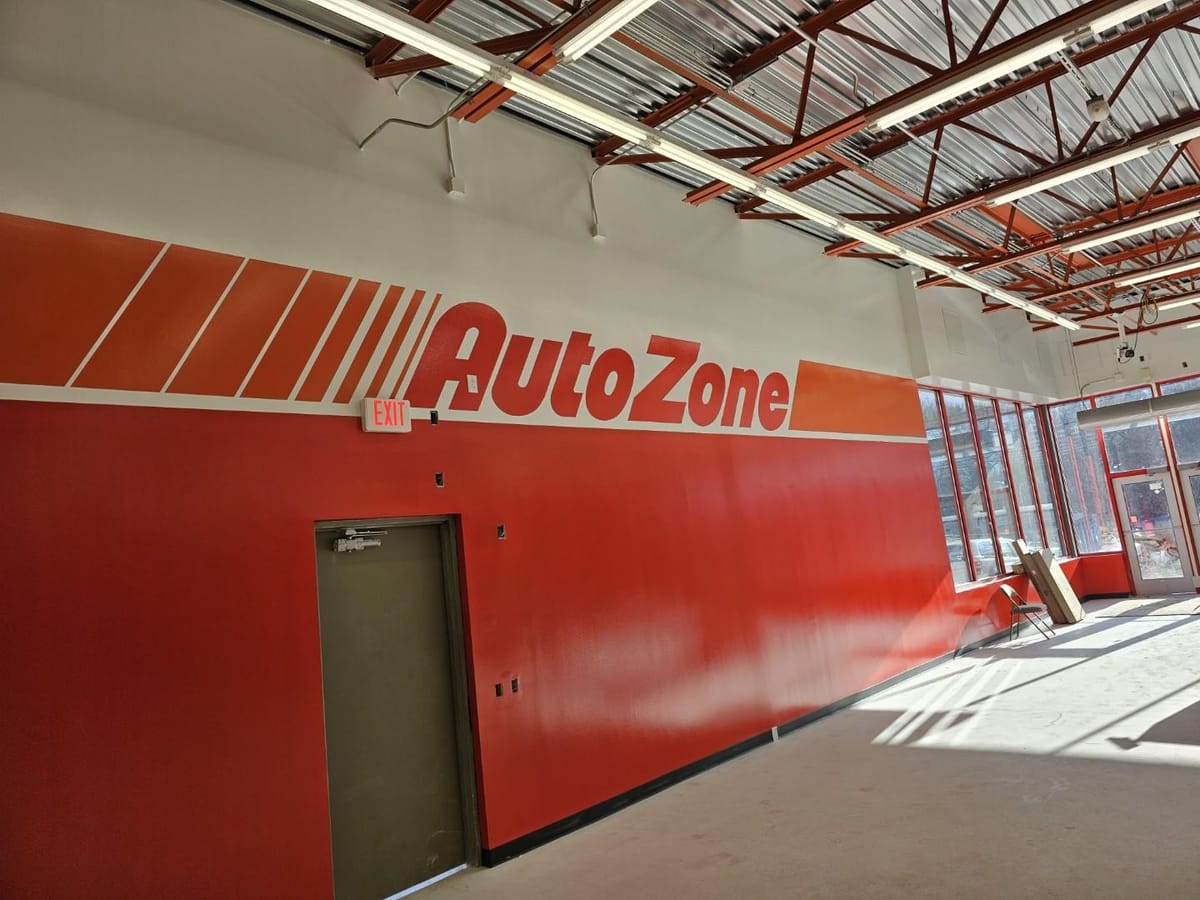 Finished AutoZone sales floor, the full painted brand logo and orange band running the length of the red wall