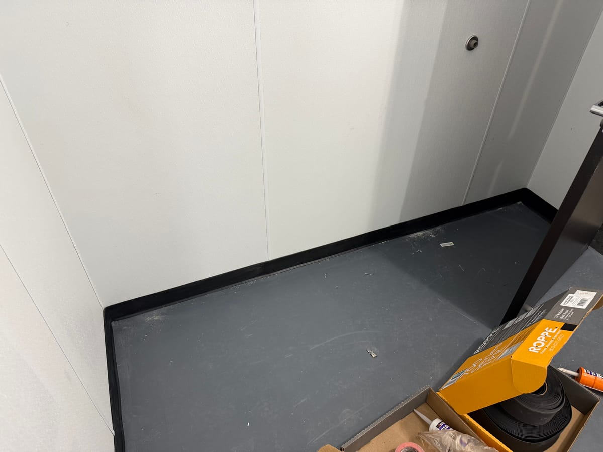 Finished interior wall panel and black rubber base trim installed at a new Dollar General store, with boxed floor trim material staged nearby