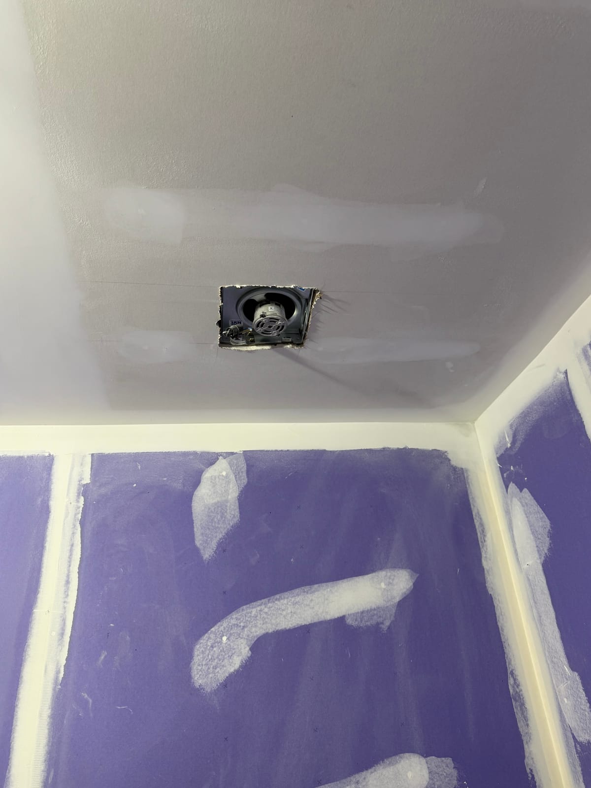 Finished drywall ceiling and taped seams around a new exhaust fan cutout, with moisture-resistant purple board on the adjoining walls