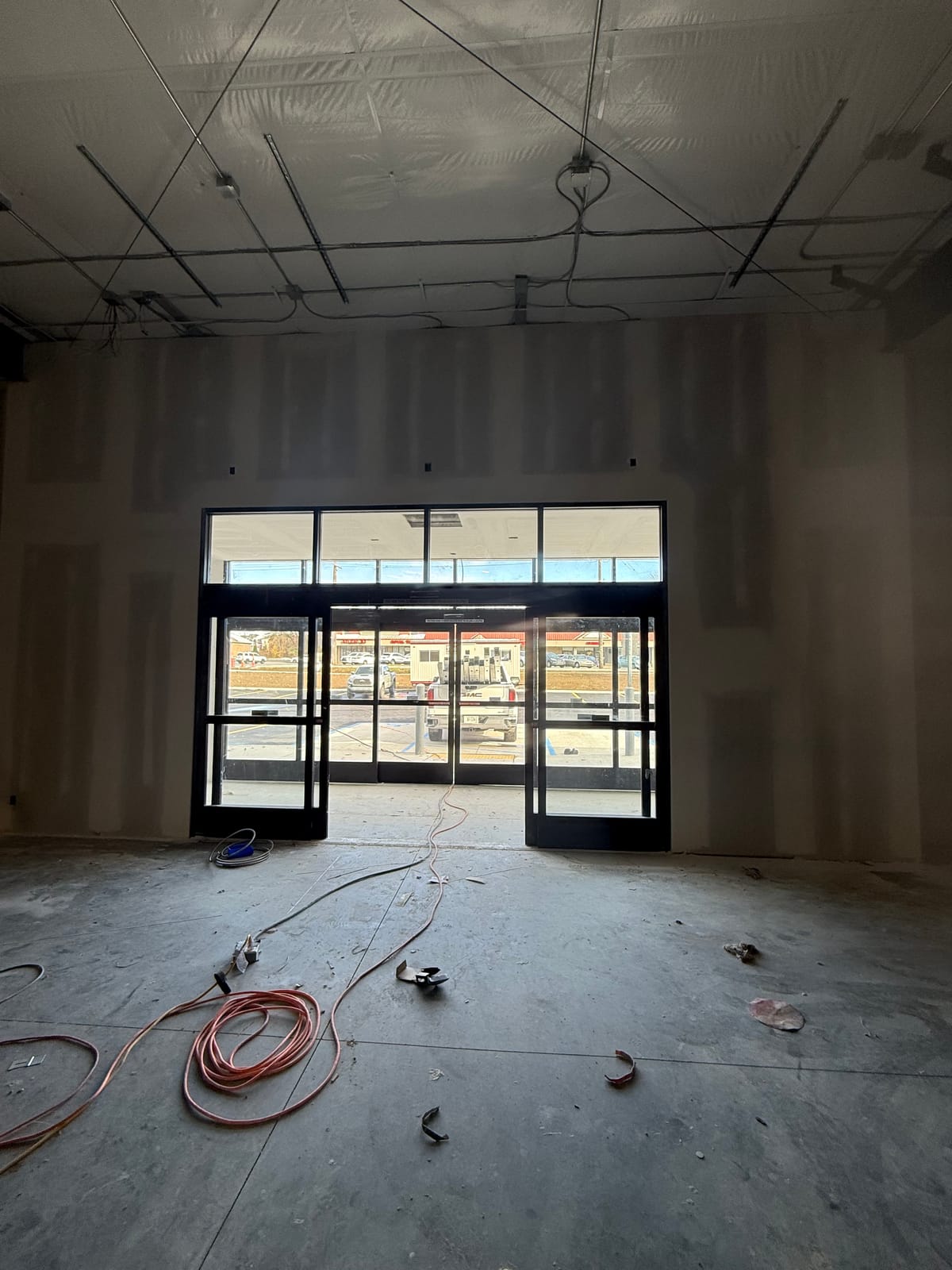 Hung and taped drywall walls at a new storefront entry, with electrical wire stubbed for outlets and structural steel deck visible above