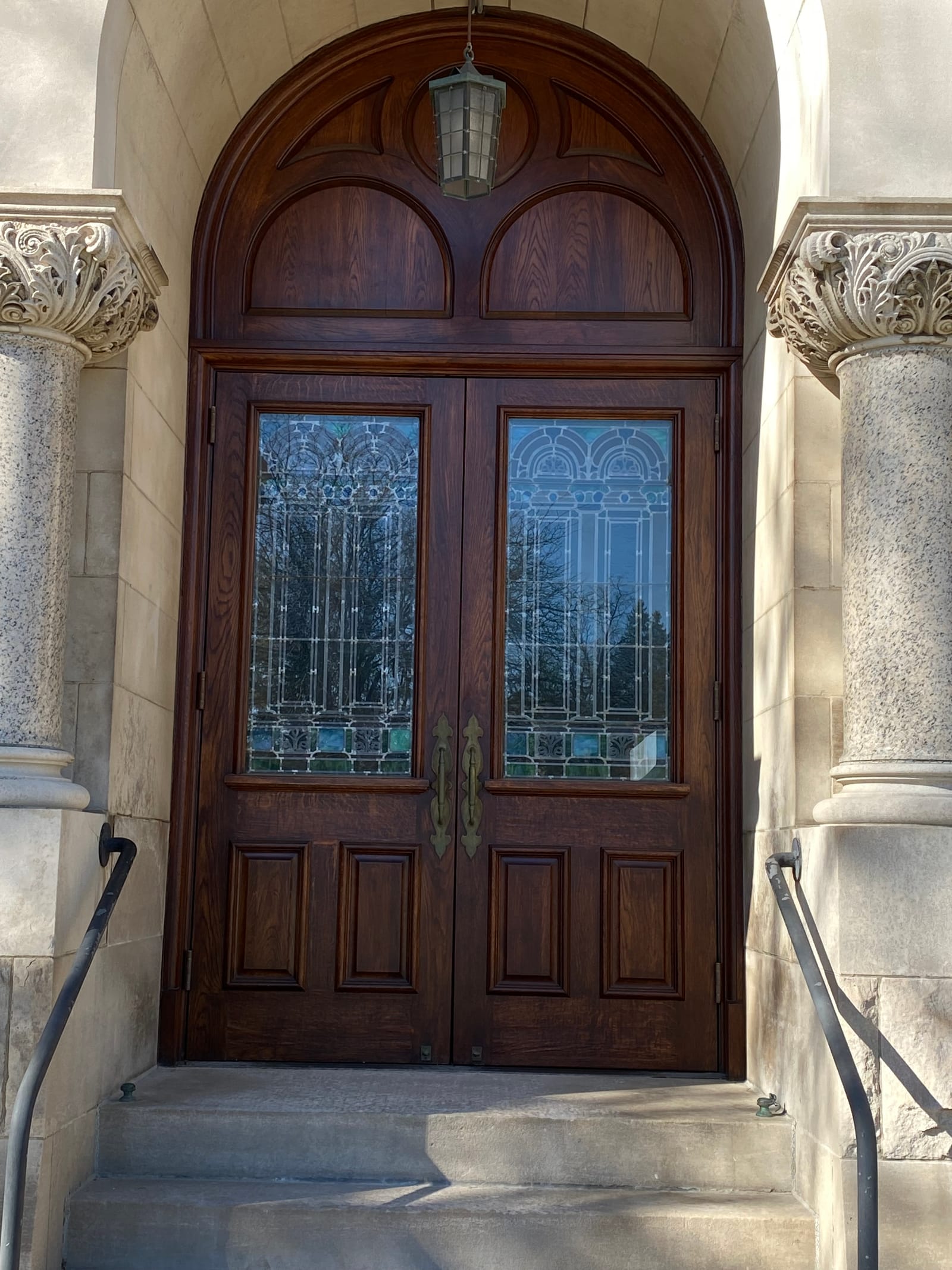 Restored oak arched double doors with their original stained glass, framed by the carved stone entry of a 116-year-old building