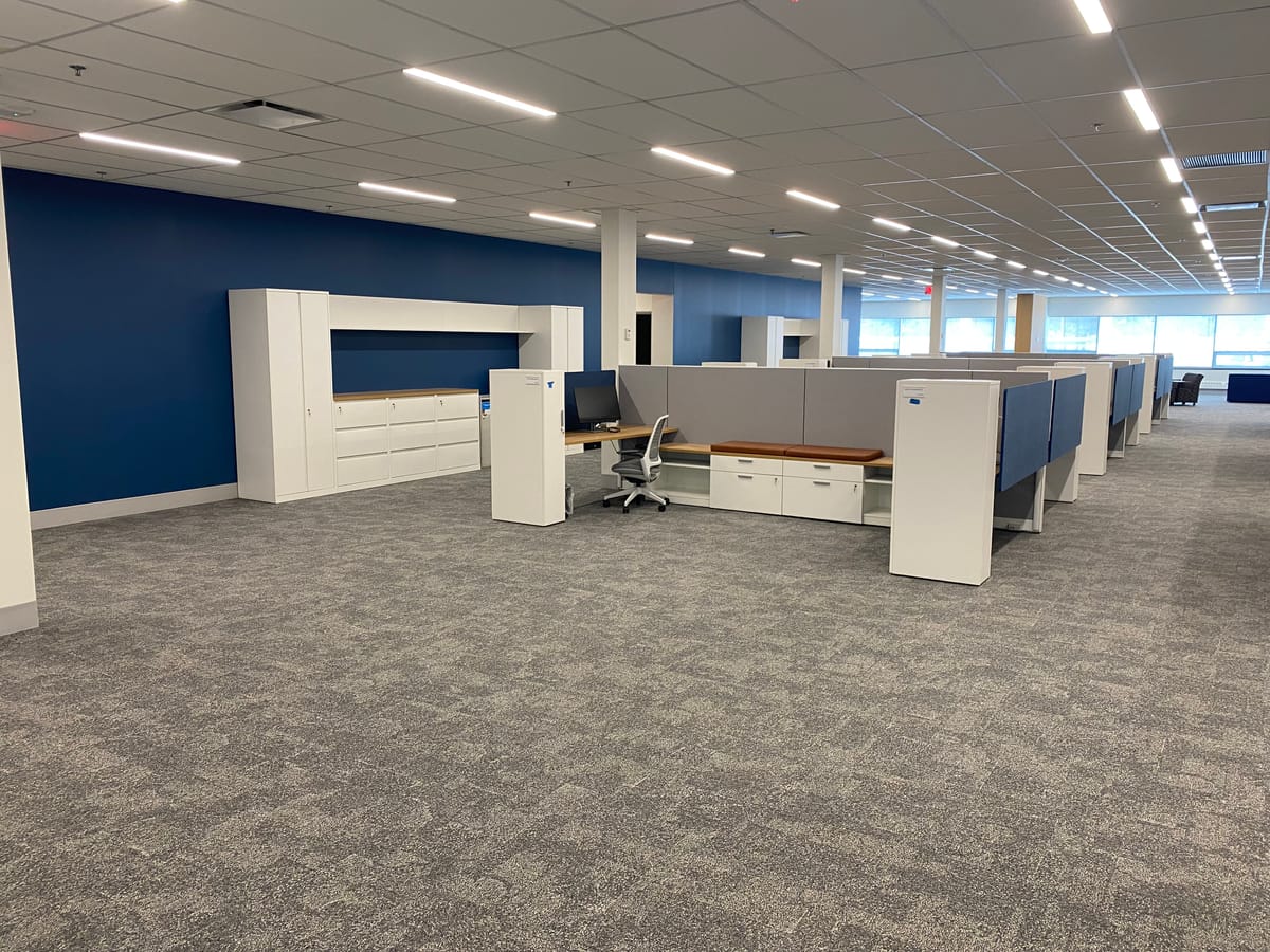 Finished open office with a blue accent wall, storage cabinetry, and a suspended ceiling grid overhead