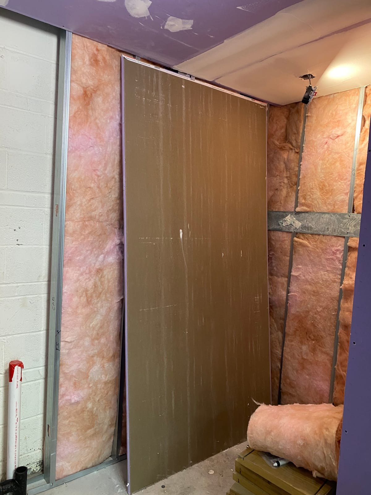 Steel stud framing with fiberglass batt insulation and a moisture-resistant board panel staged against an existing CMU wall