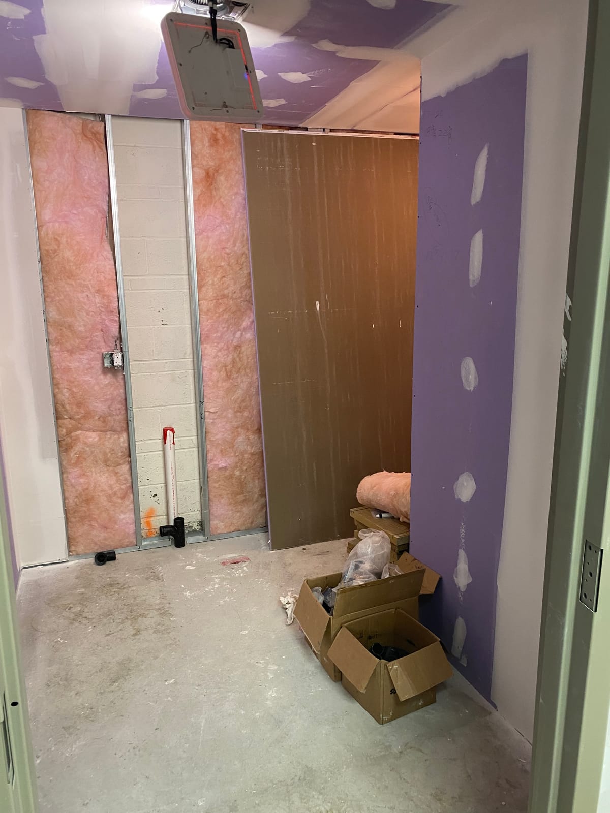 Steel stud track and studs against an existing CMU wall, with fiberglass batt insulation installed between studs and moisture-resistant board staged for a corporate office build-out