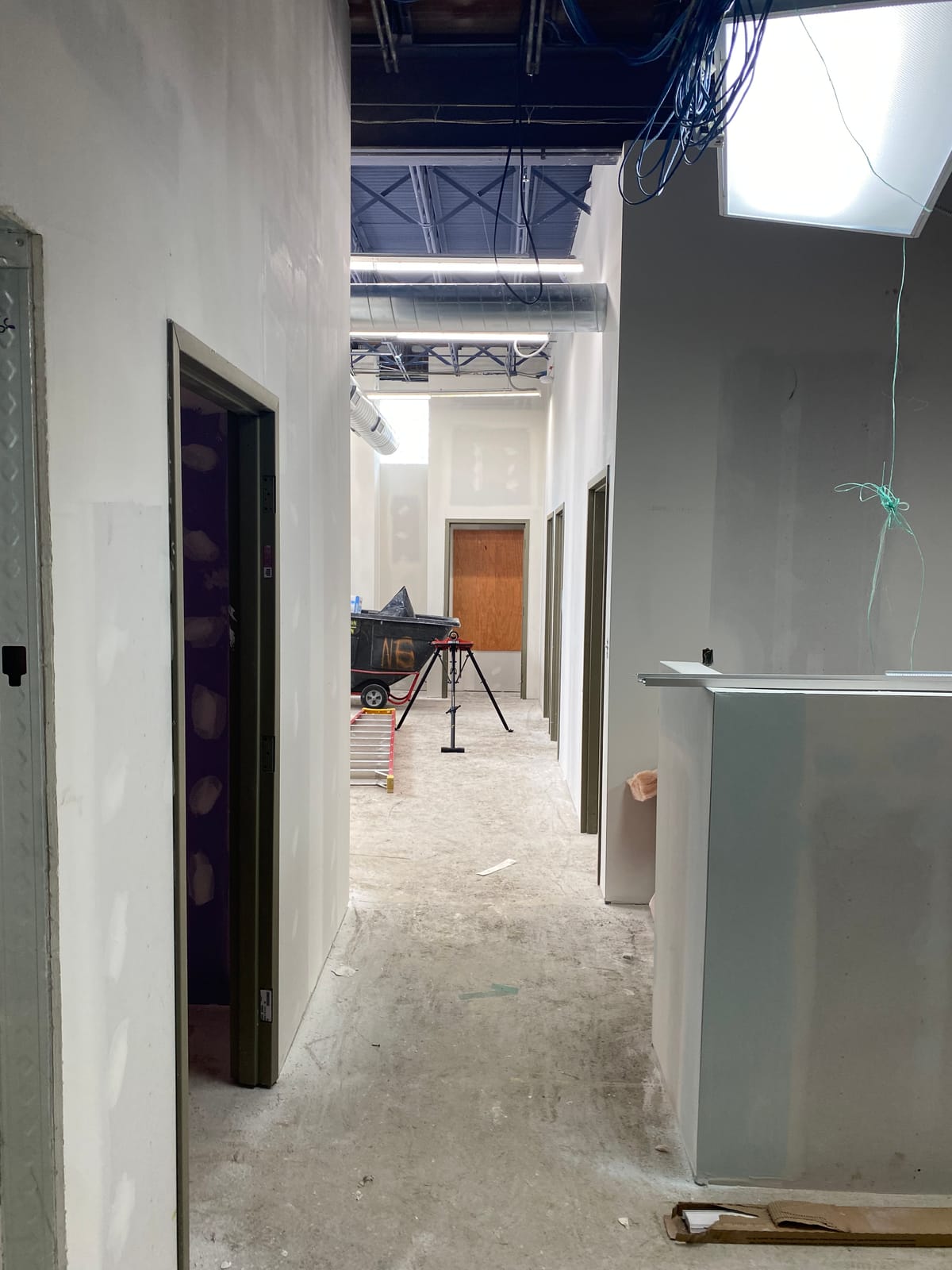 Corridor mid-construction with framed drywall partitions, a metal door frame, and open ceiling structure above