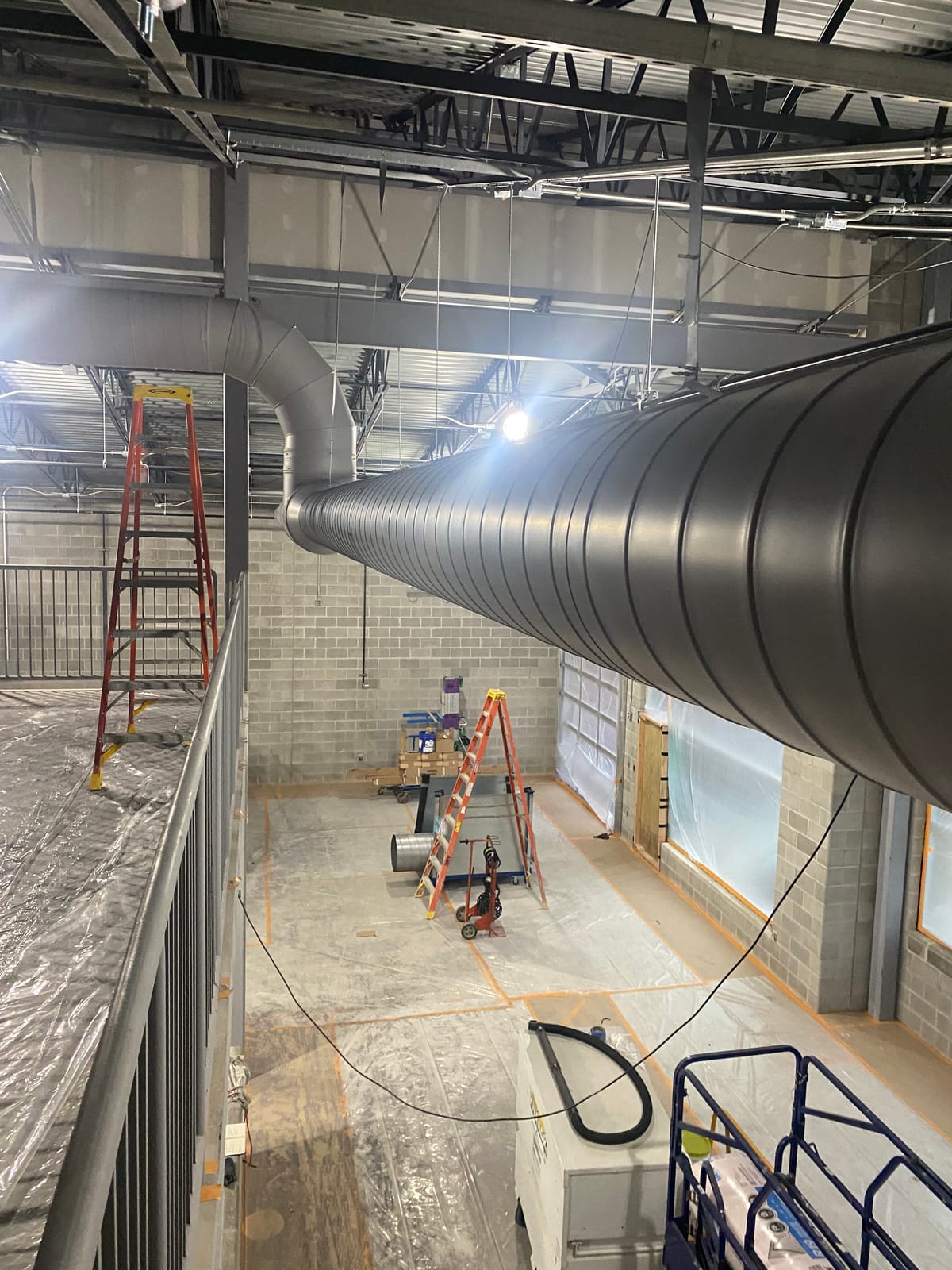 Painted block walls and structural steel in a high-bay classroom addition at Theodore Roosevelt High School, mid-renovation with floor protection and ladders staged